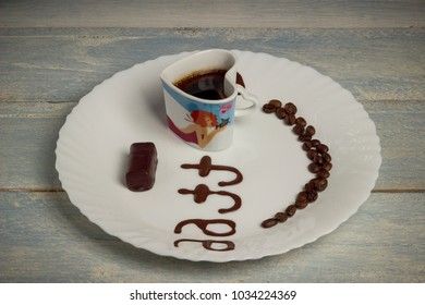 black grain coffee with chocolate candy on a white plate with a wooden background and an inscription