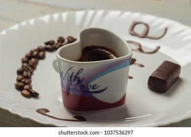 black grain coffee with chocolate candy on a white plate with a wooden background and an inscription