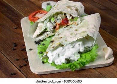 Shaurma, cut in half, meat with vegetables in a bread cake on an old wooden rustic background, on a wooden board with tomato and pepper