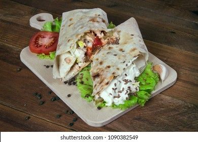 Shaurma chicken roll in a pita with fresh vegetables and cream sauce composition on wooden background