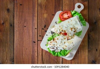 Shaurma, cut in half, meat with vegetables in a bread cake on an old wooden rustic background, on a wooden board with tomato and pepper
