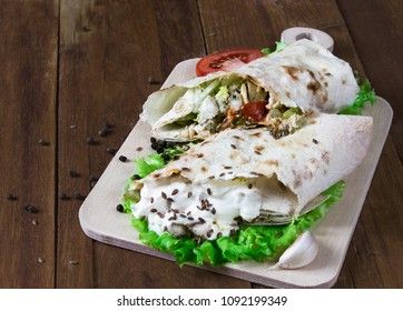 Shaurma, cut in half, meat with vegetables in a bread cake on an old wooden rustic background, on a wooden board with tomato and pepper