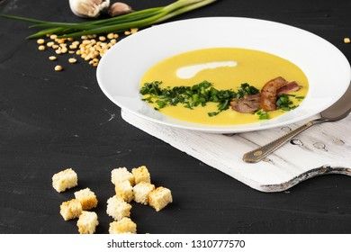 Pea soup with pieces of bacon, parsley and onion in a bowl on a dark background. Pea cream soup.