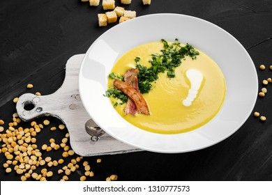 Pea soup with pieces of bacon, parsley and onion in a bowl on a dark background. Pea cream soup.