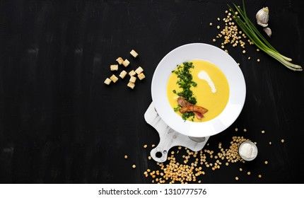 Pea soup with bacon and croutons on a dark background, top view. Yellow cream soup puree with greens.