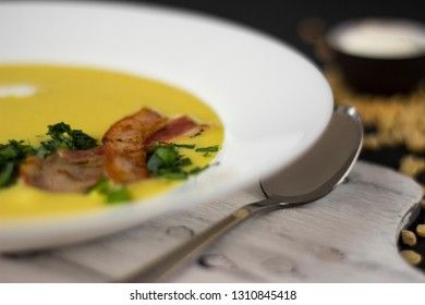 Pea soup with pieces of bacon, parsley and onion in a bowl on a dark background. Pea cream soup. Macro