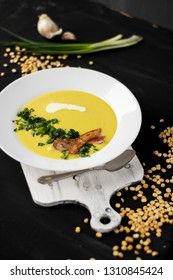 Pea soup with pieces of bacon, parsley and onion in a bowl on a dark background. Pea cream soup.