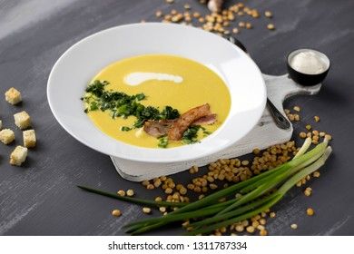 Pea soup with pieces of bacon, parsley and onion in a bowl on a gray background. Pea cream soup.