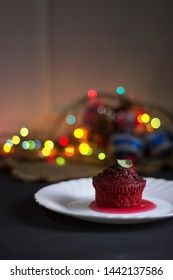 Red cupcake with chocolate chips on a dark background with multi-colored bokeh